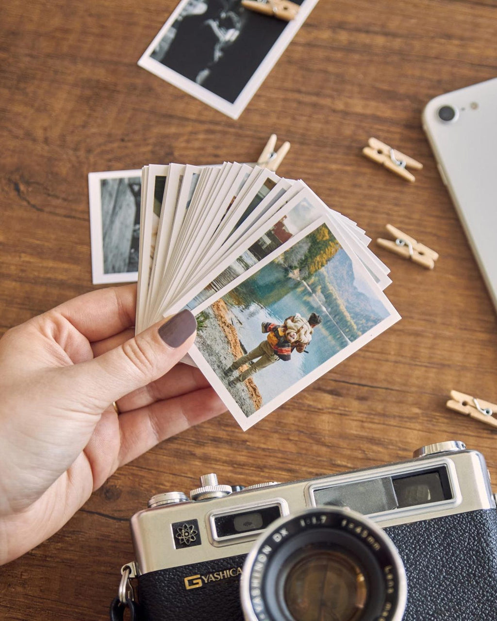 Hand holding a stack of small photos next to a vintage camera on a wooden surface.