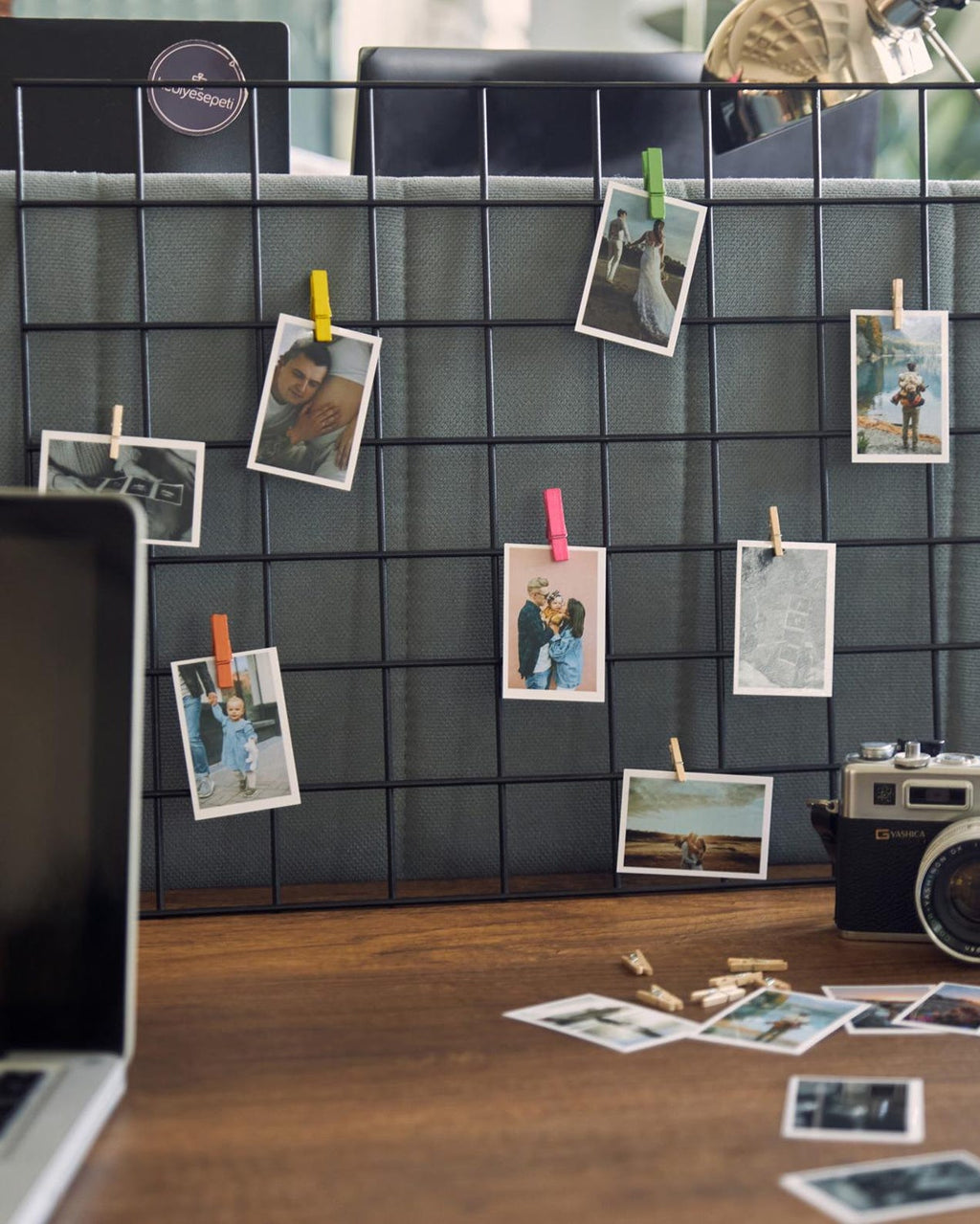 Grid wall with photos pinned to it, next to a camera on a desk.