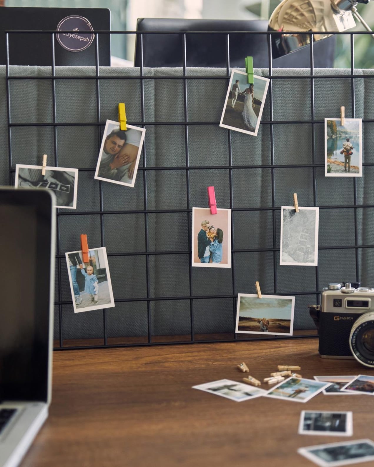 Grid wall with photos pinned to it, next to a camera on a desk.