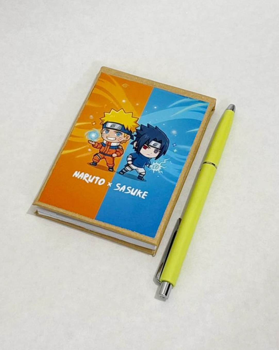 Notebook with Naruto and Sasuke design and a yellow pen on a white background