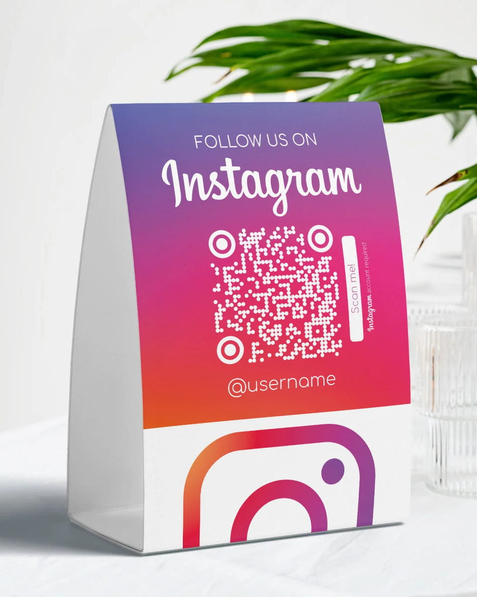 Colorful stand with Instagram QR code and username on a white surface with a plant in the background